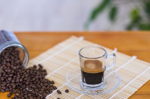 Black coffee in glass cup and coffee beans on the wooden table